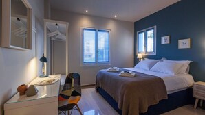 A bedroom with a bed, bedside tables, a chair, a desk, and a mirror. - Thalias Quarters - Kalamata Mediterranean Suites & Villas (Kalamata)