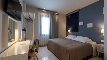A hotel room with a bed, a desk with a mirror, a chair, a TV, and a window with curtains.
