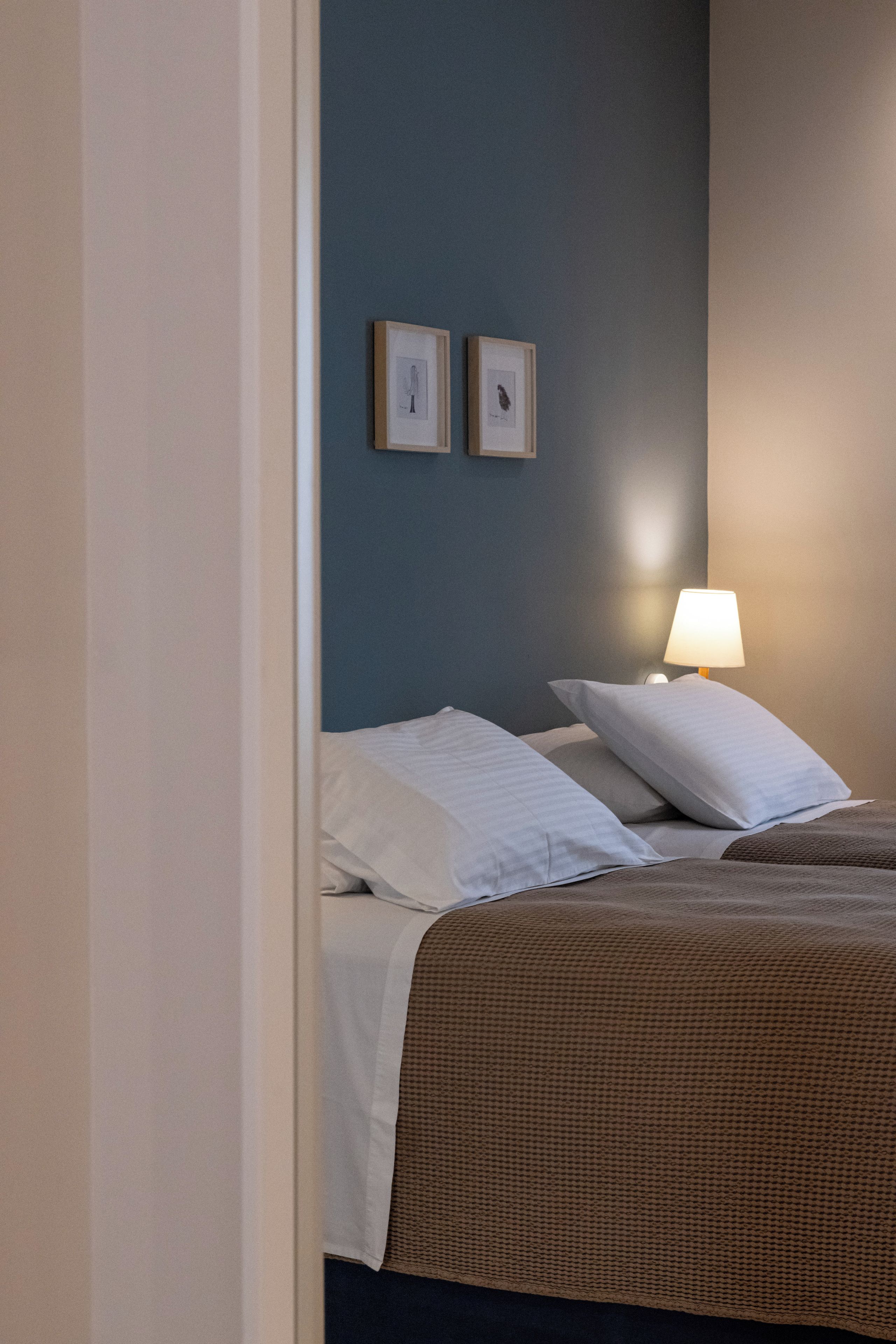 A bedroom with a bed, pillows, a lamp, and two framed pictures on the wall.