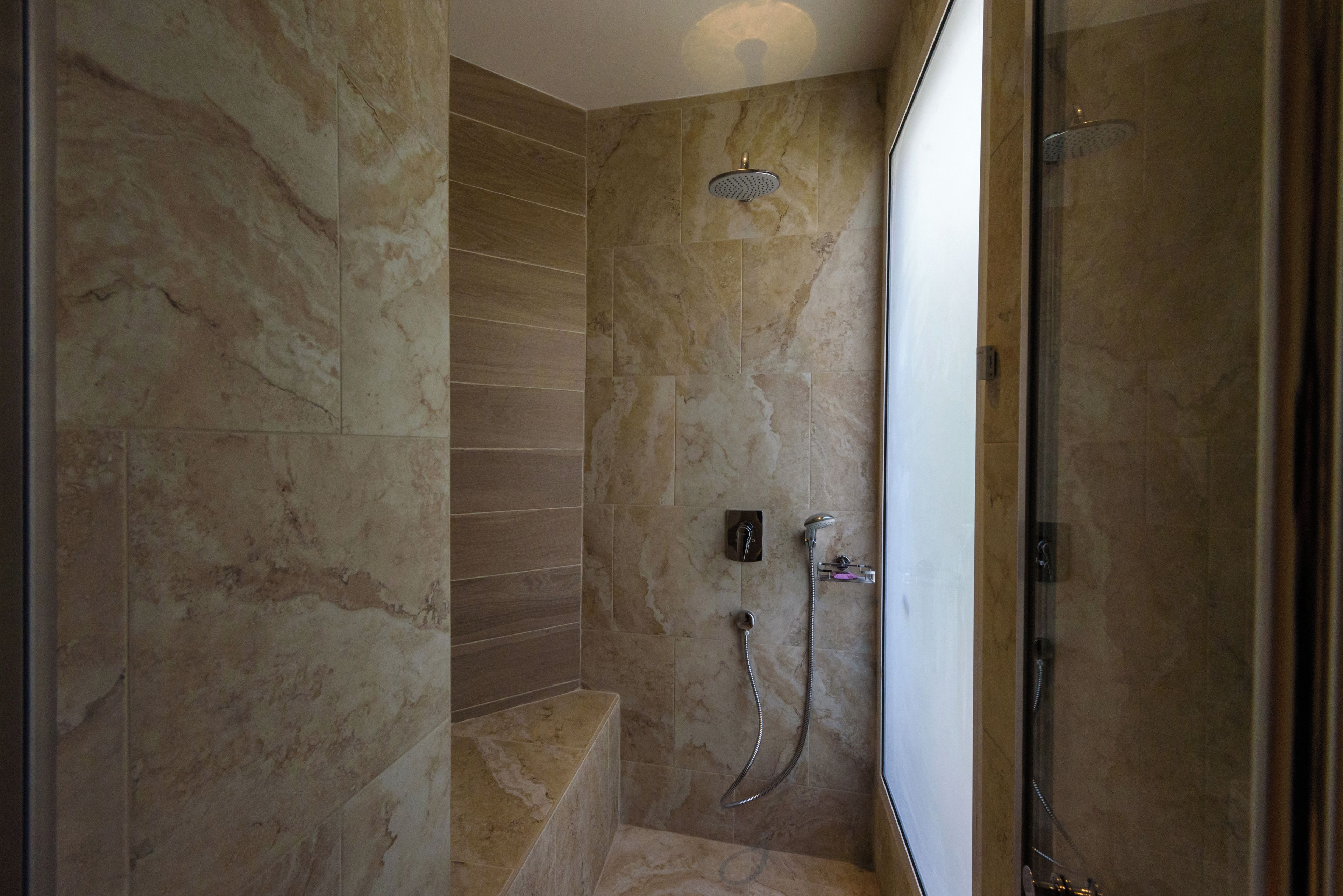 A modern bathroom with a glass shower enclosure, marble walls, and a built-in bench.