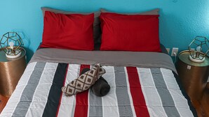 A bed with a striped bedspread, two red pillows, and a pair of slippers on the bed. There are two bedside tables with lamps and a wall with three framed pictures. - Heart of South Beach ¤ 2 min Plage ¤ Ocean Drive (Miami Beach)