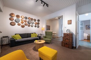 A living room with a sofa, two yellow armchairs, a coffee table, and a wall of decorative plates. - Greenhouse - Kalamata Mediterranean Suites & Villas (Kalamata)