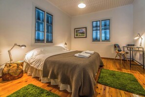 A bedroom with a bed, two windows with blinds, a desk with a chair, and a green rug. - Greenhouse - Kalamata Mediterranean Suites & Villas (Kalamata)