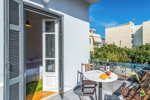 Un balcon avec un lit, une table sur laquelle se trouvent une bouteille et une pomme, et une chaise.