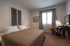 A hotel room with a bed, a desk, a chair, a lamp, and a picture on the wall. - Greenhouse - Kalamata Mediterranean Suites & Villas (Kalamata)