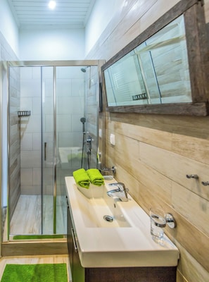 A modern bathroom with a glass shower enclosure, a white sink with a mirror, and a wooden vanity. - Greenhouse - Kalamata Mediterranean Suites & Villas (Kalamata)