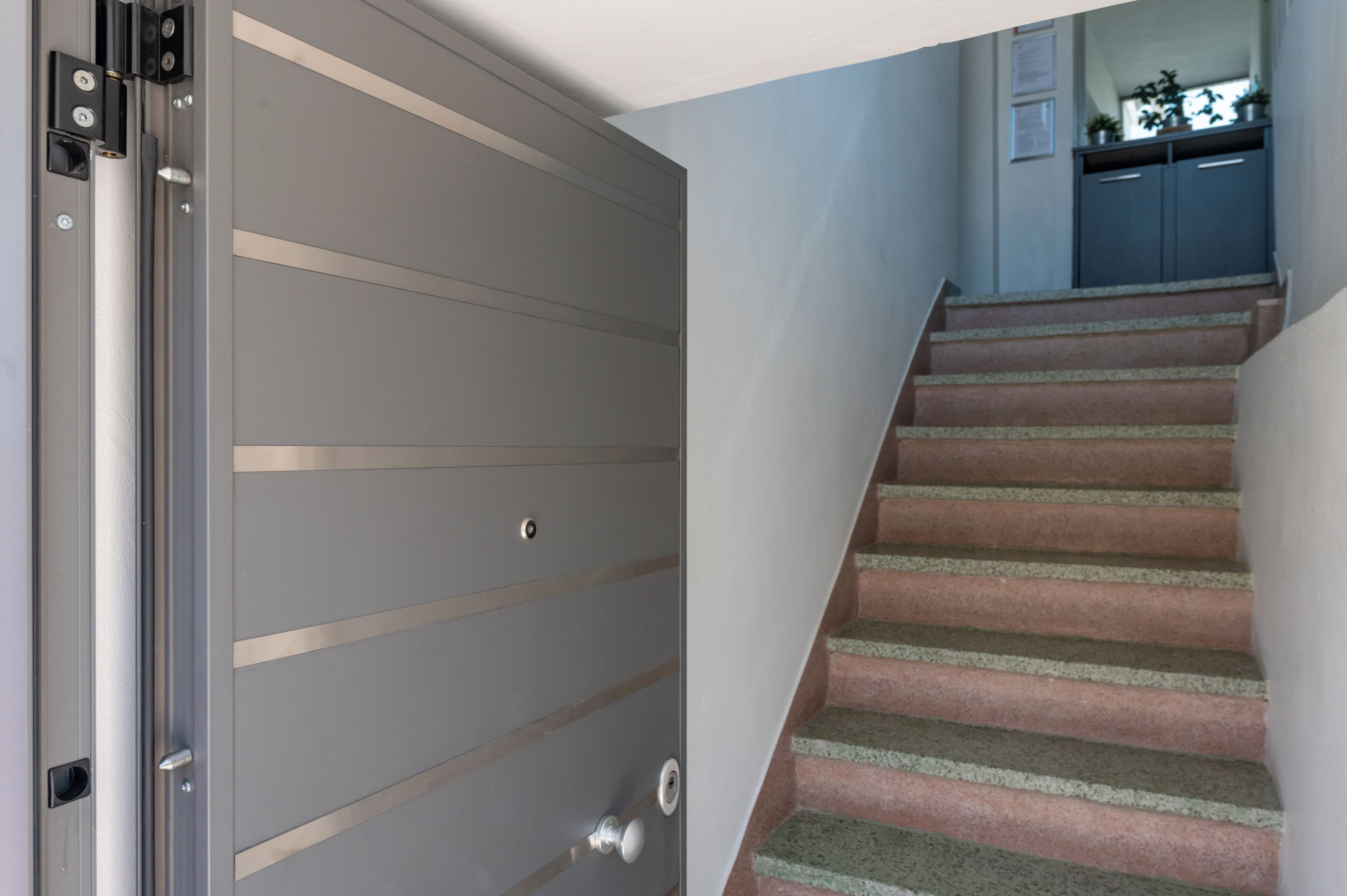 Una porta scorrevole chiusa con maniglia metallica e una serratura, una scala con pianerottolo rivestito di moquette, e una zona cucina con pensili e un piano di lavoro.