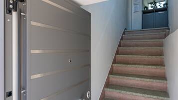 Una porta scorrevole chiusa con maniglia metallica e una serratura, una scala con pianerottolo rivestito di moquette, e una zona cucina con pensili e un piano di lavoro.