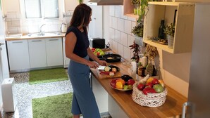 A kitchen with a person preparing food, a sink, a toaster, and a fruit basket on the counter. - Greenhouse - Kalamata Mediterranean Suites & Villas (Kalamata)
