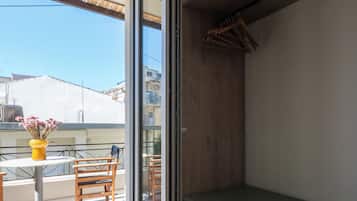 A room with a sliding glass door leading to a balcony with wooden furniture and a yellow vase with flowers.