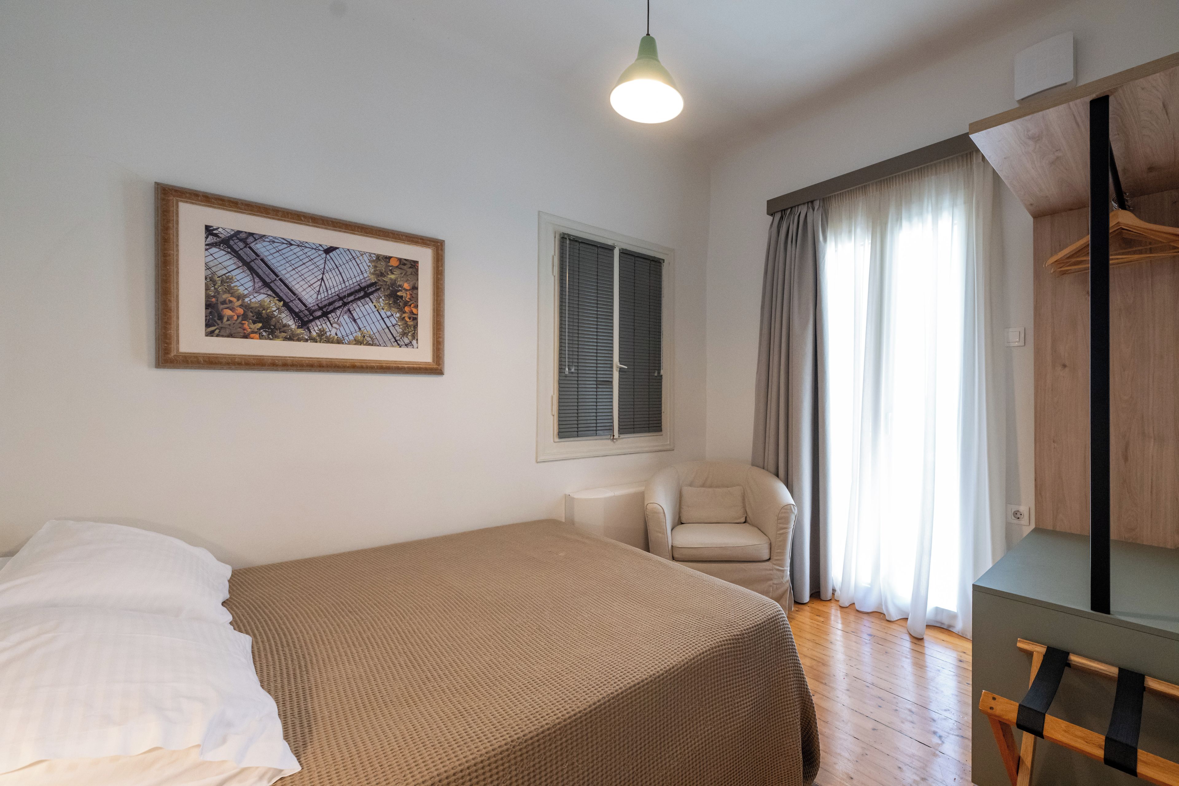 A bedroom with a bed, a chair, a desk, a hanging light, and a window with curtains.