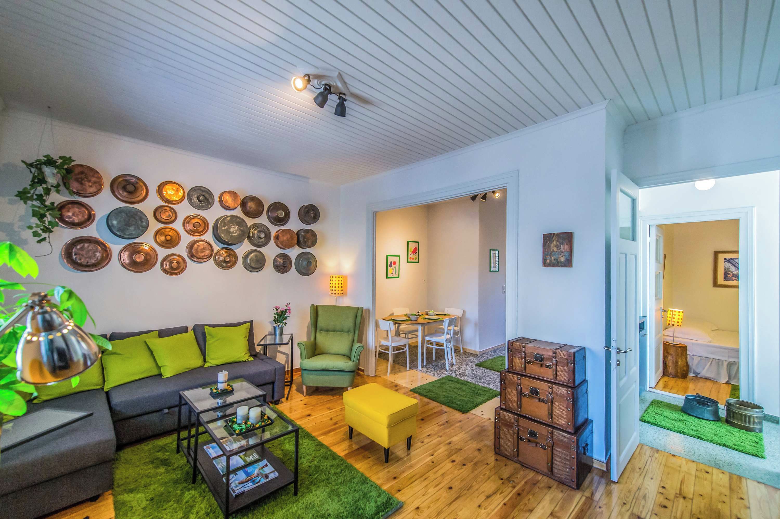 Ein Wohnzimmer mit Sofa, Sessel, Couchtisch und einem Essbereich mit Tisch und Stühlen. An den Wänden befinden sich Dekorationen und es gibt einen Deckenventilator.