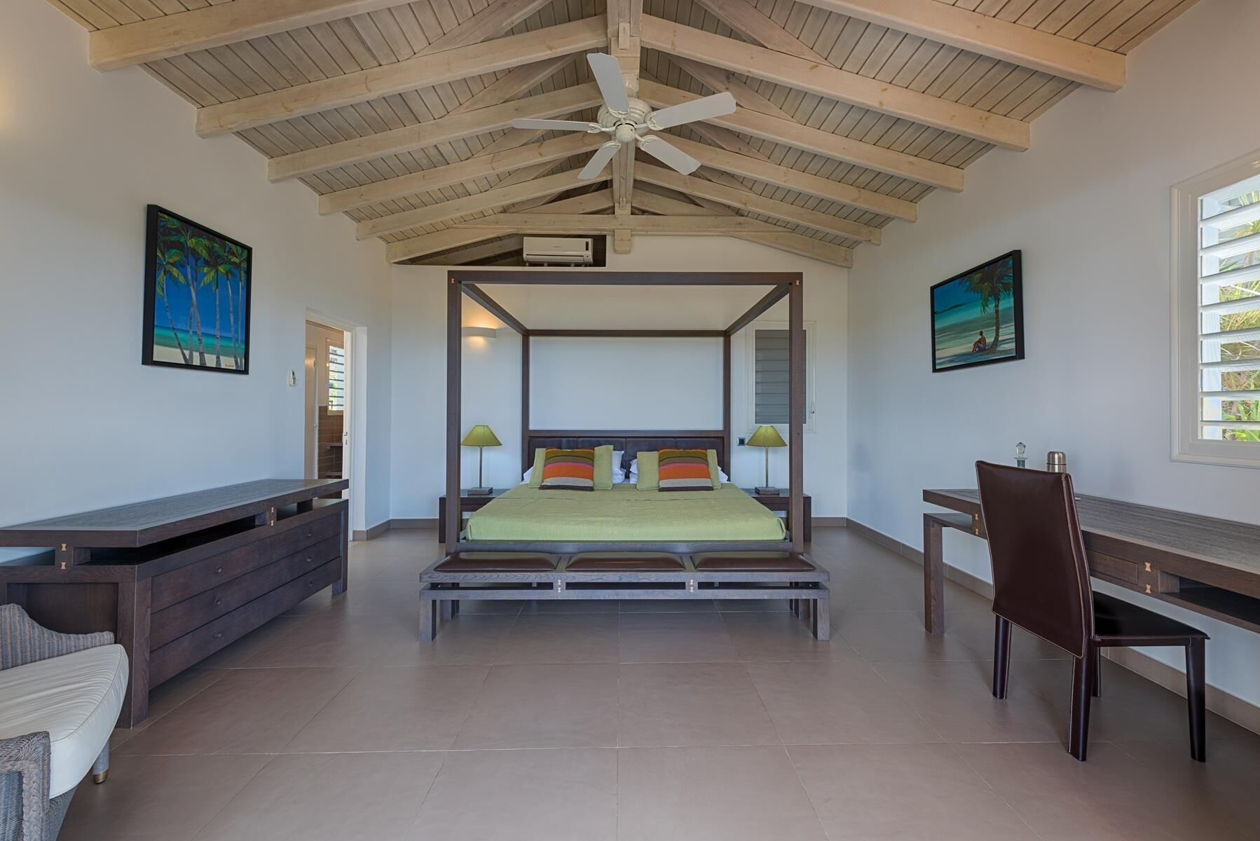 A spacious bedroom with a four-poster bed, a desk, and a chair.