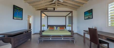 A spacious bedroom with a four-poster bed, a desk, and a chair.