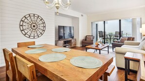 Una sala de estar moderna con una mesa de comedor de madera, un televisor y un balcón con mobiliario exterior.