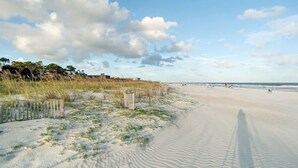 Una playa con arena, una valla de madera y una fila de árboles al fondo.