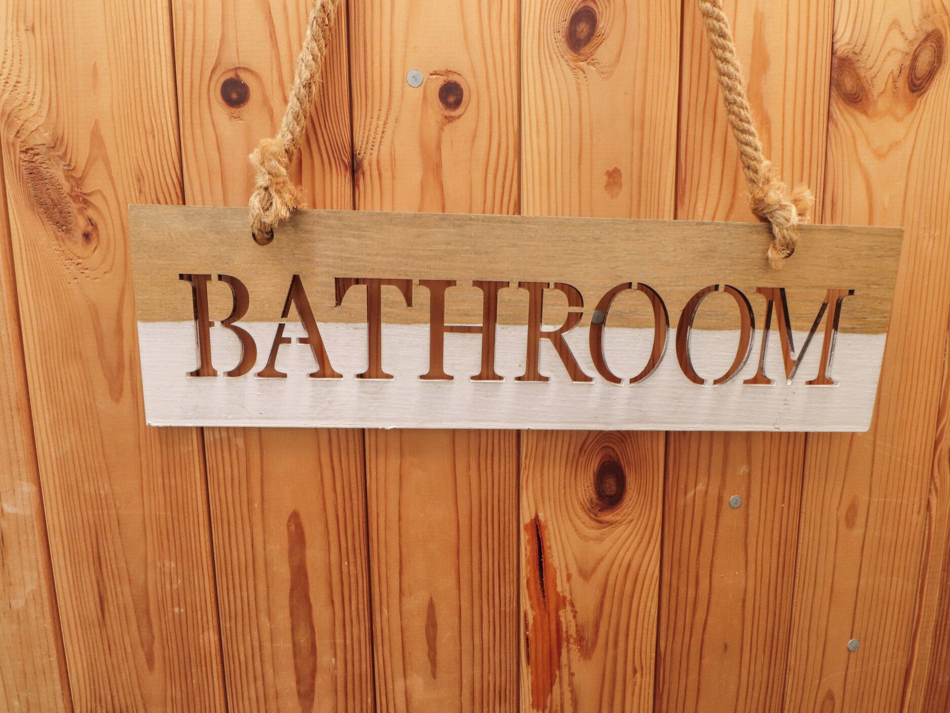 Une pancarte en bois portant l’inscription « SALLE DE BAINS » est accrochée à un mur en bois.