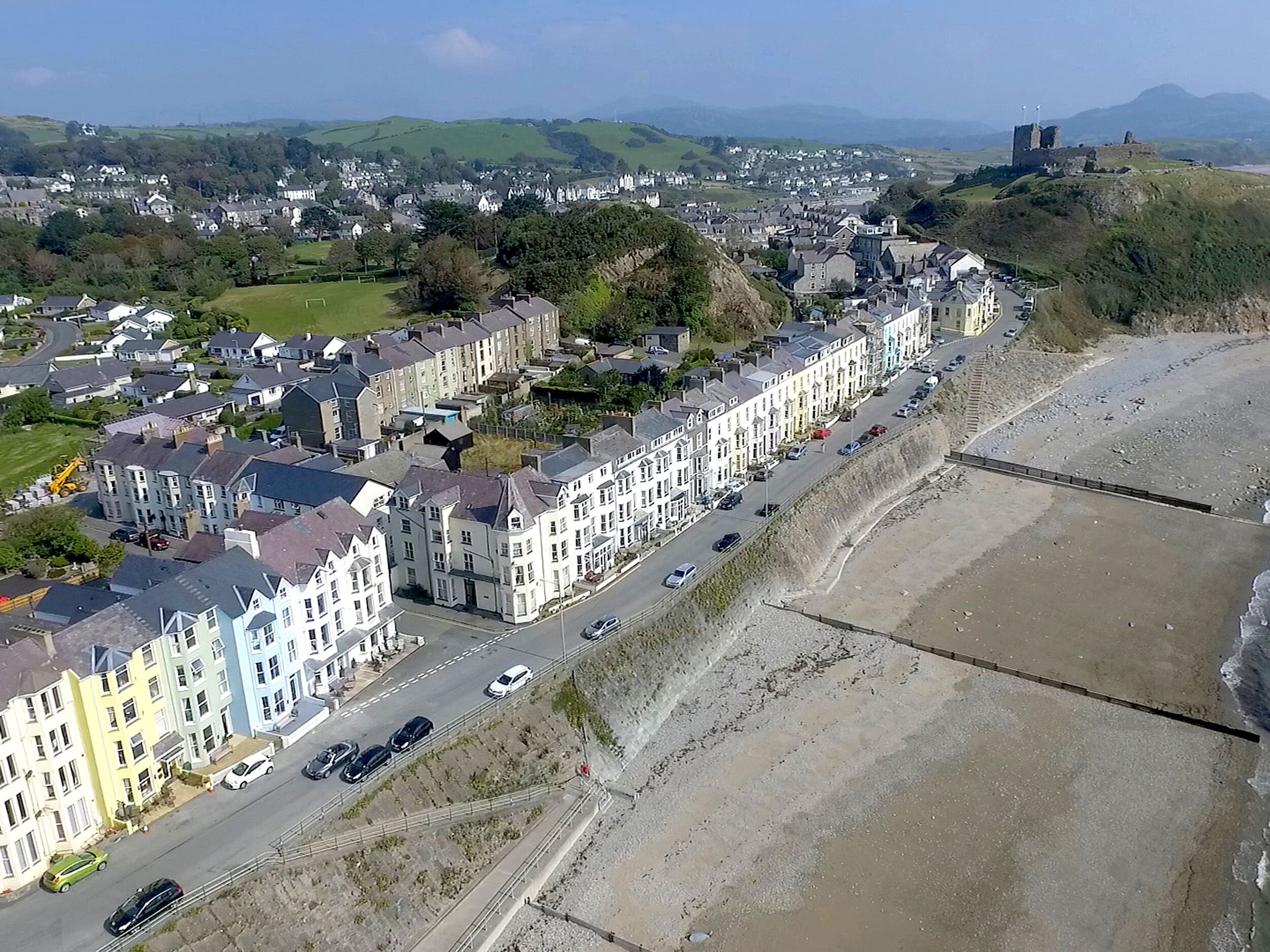 A coastal town with terraced houses along the beach, a clear road, and a distant castle.