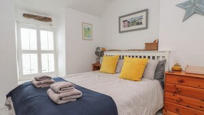 Un dormitorio con cama, mesita de noche, cómoda, adorno con forma de estrella, cuadro enmarcado y ventana con persianas.