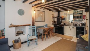 Una sala de estar acogedora con un sofá, una mesa de comedor con sillas, una cocina con estufa y un reloj en la pared.