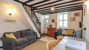 Una sala de estar acogedora con una escalera, un sofá, un armario de madera y una mesa de comedor con un cuaderno.