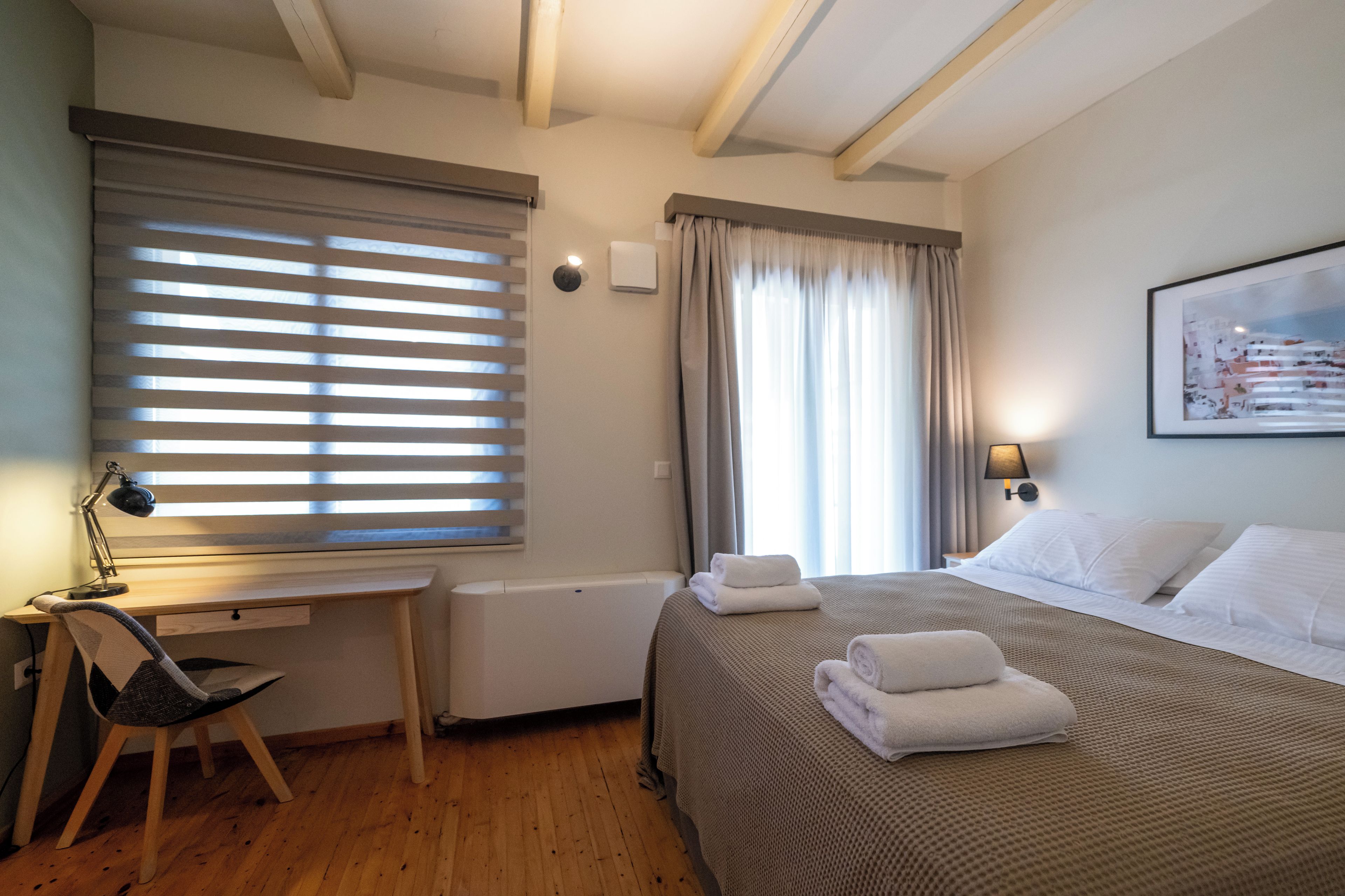 Une chambre d’hôtel avec un lit, un bureau et une chaise, un radiateur et une fenêtre avec des stores.