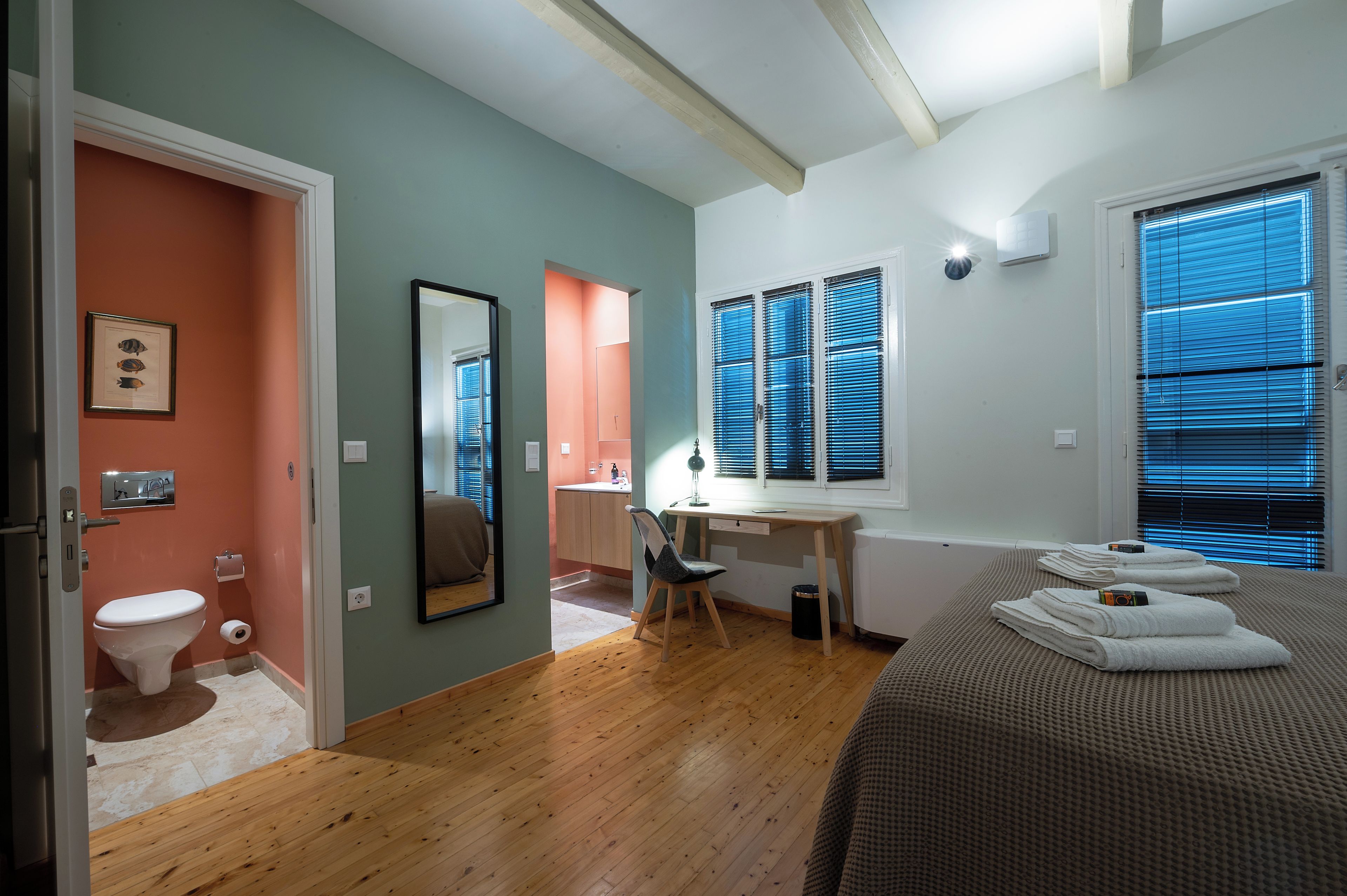 Ein Schlafzimmer mit Bett, Schreibtisch, Stuhl, Toilette und einem Fenster mit Jalousien.