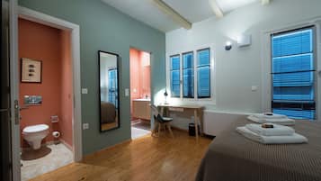 Ein Schlafzimmer mit Bett, Schreibtisch, Stuhl, Toilette und einem Fenster mit Jalousien.