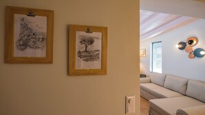 A room with a white sofa, two framed drawings on the wall, and a ceiling with exposed beams. - Tinas Home - Kalamata Mediterranean Suites & Villas (Kalamata)