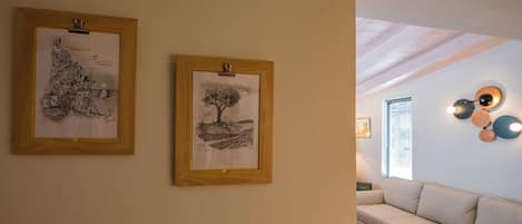 Ein Zimmer mit einem weißen Sofa, zwei gerahmten Zeichnungen an der Wand und einer Decke mit freiliegenden Balken.