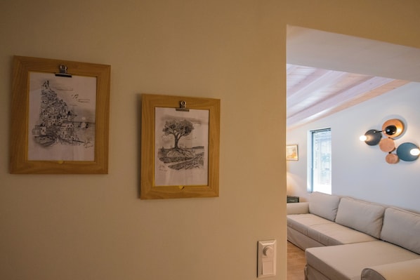 Une pièce avec un canapé blanc, deux dessins encadrés accrochés au mur et un plafond avec des poutres apparentes.