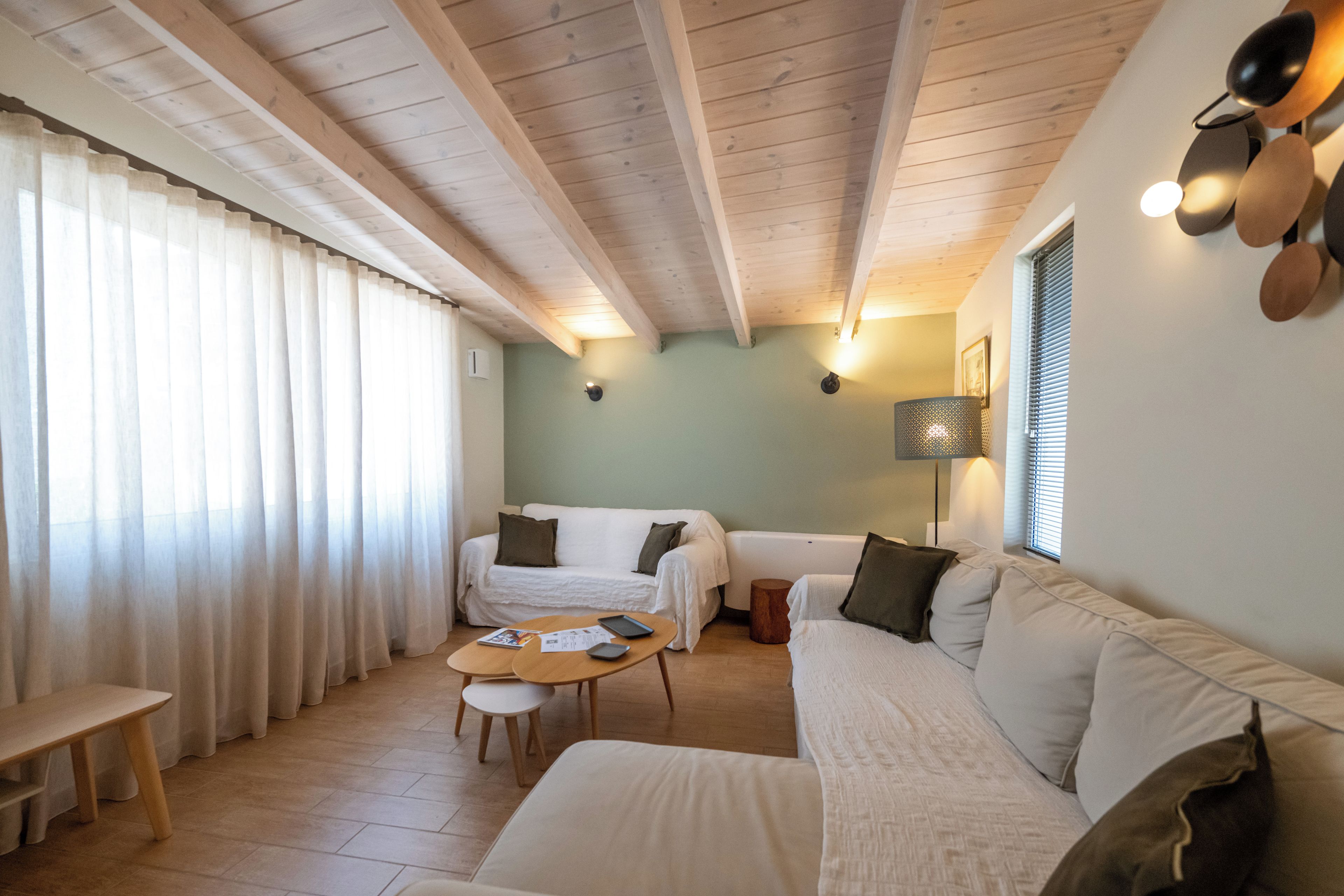 A cozy room with a wooden ceiling, a sofa, a small table, and a window with curtains.