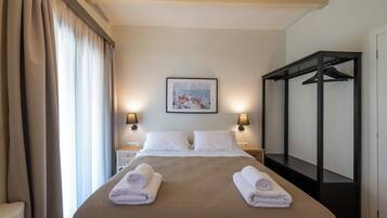 A hotel room with a bed, two bedside tables, a wall-mounted painting, a black wardrobe, and a window with curtains.