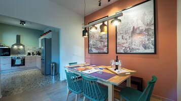 A modern kitchen with a dining area, featuring a granite countertop, stainless steel appliances, and a wooden dining table with teal chairs.