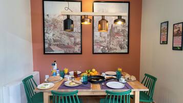 A dining area with a wooden table set for breakfast, green chairs, and artwork on the walls.
