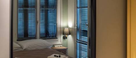 Una habitación de hotel con cama, mesita de noche, lámpara y ventana con persianas.