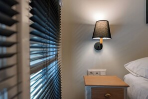 A bedroom with a bedside table, a lamp, and a window with blinds. - Tinas Home - Kalamata Mediterranean Suites & Villas (Kalamata)