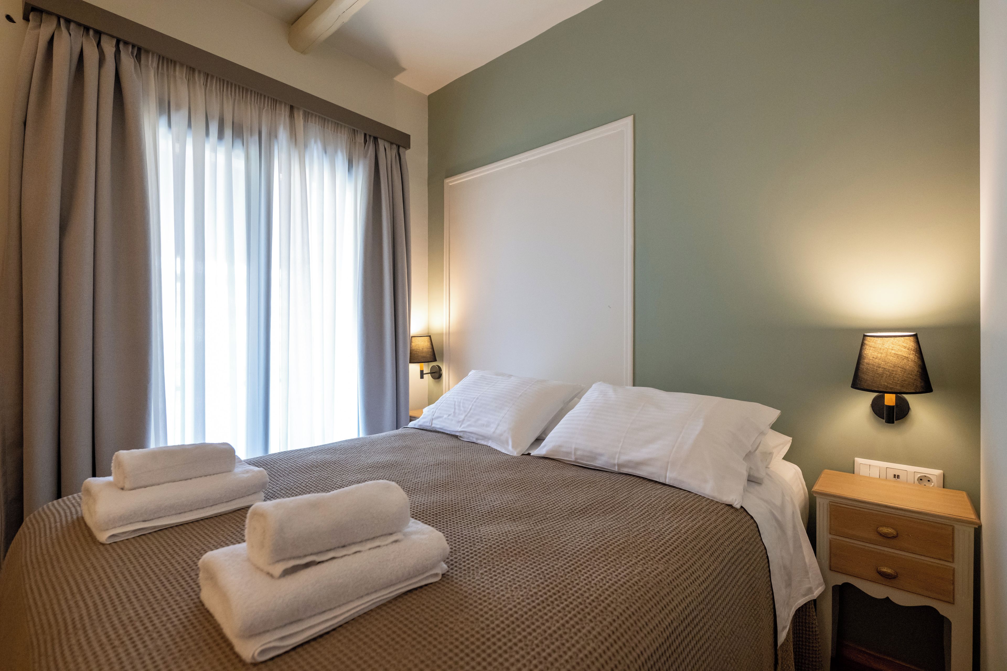 A neatly made bed with white linens, a bedside lamp, and a nightstand with a drawer.