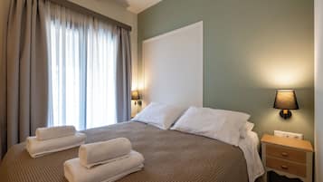 A neatly made bed with white linens, a bedside lamp, and a nightstand with a drawer.