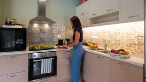 A kitchen with a stove, oven, and a person preparing food. - Tinas Home - Kalamata Mediterranean Suites & Villas (Kalamata)