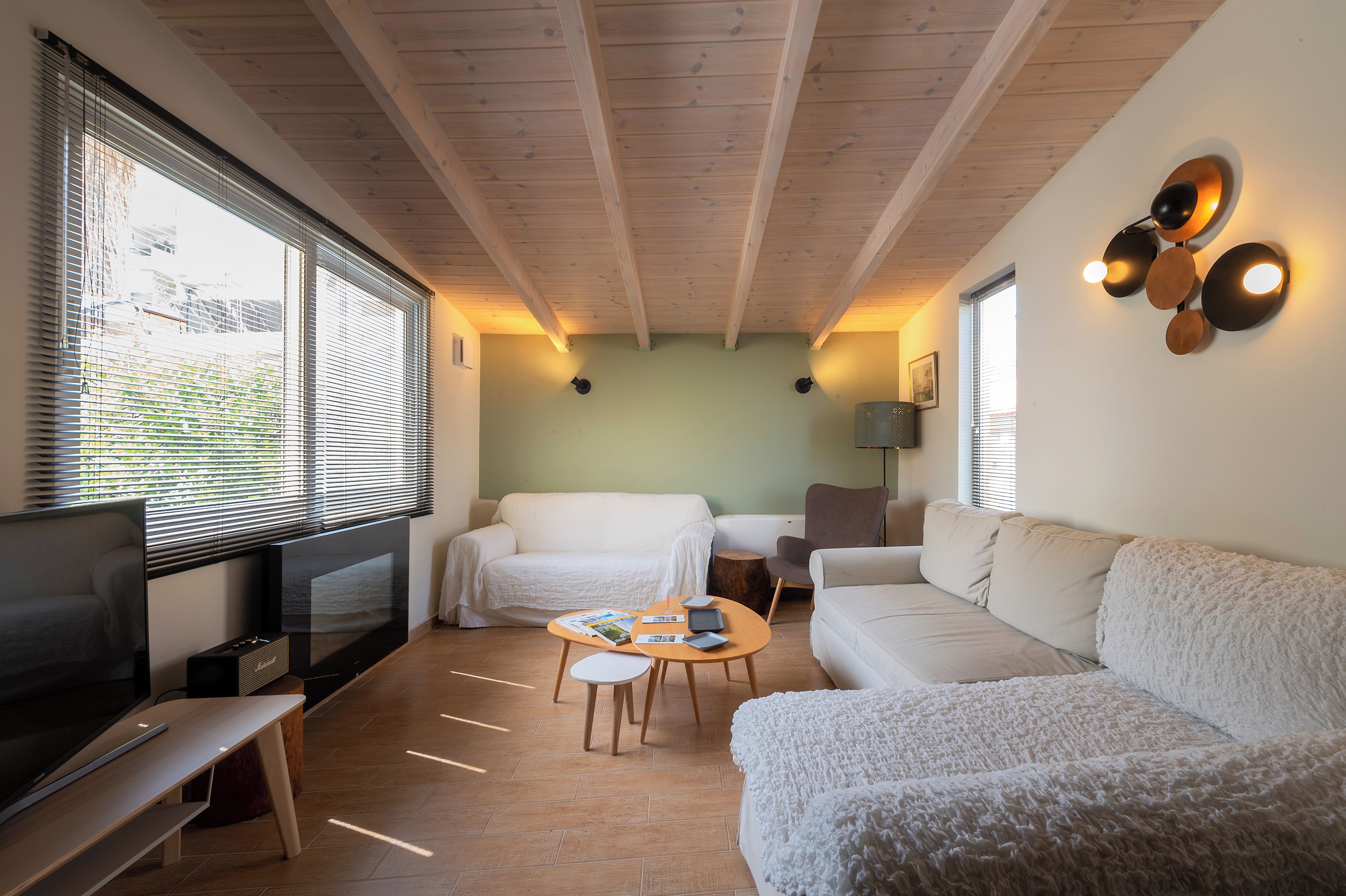 Ein modernes Wohnzimmer mit Flachbildfernseher, einer Couch, einem Couchtisch und einem Fenster mit Jalousien.