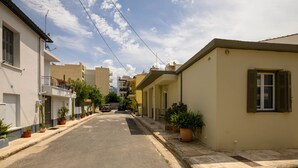 A narrow street lined with residential buildings, potted plants, and a parked car. - Tinas Home - Kalamata Mediterranean Suites & Villas (Kalamata)