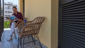 A person sitting on wicker chairs on a balcony with a book, overlooking a building with balconies. - Tinas Home - Kalamata Mediterranean Suites & Villas (Kalamata)