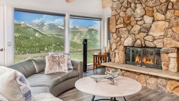 A cozy living room with a stone fireplace, a comfortable sofa, and a large window offering a mountain view. - Trails End Vacation Home At Windcliff 3 Bedroom Home by RedAwning (Estes Park)