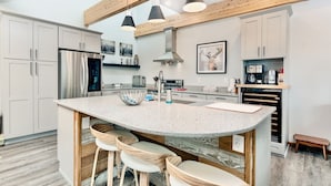 A modern kitchen with a central island, bar stools, stainless steel appliances, and wooden beams. - Trails End Vacation Home At Windcliff 3 Bedroom Home by RedAwning (Estes Park)