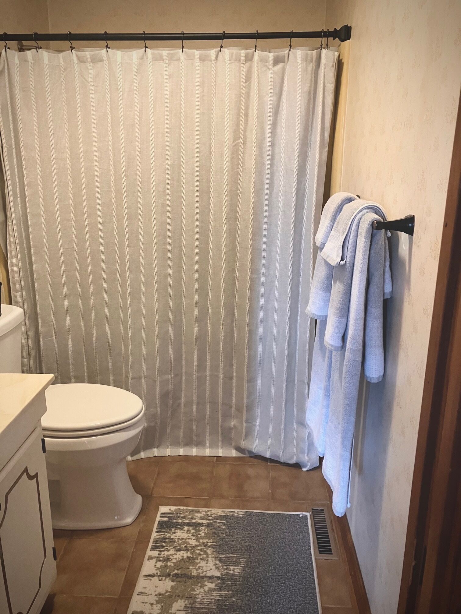 A bathroom with a toilet, a shower curtain, and a towel rack with towels.