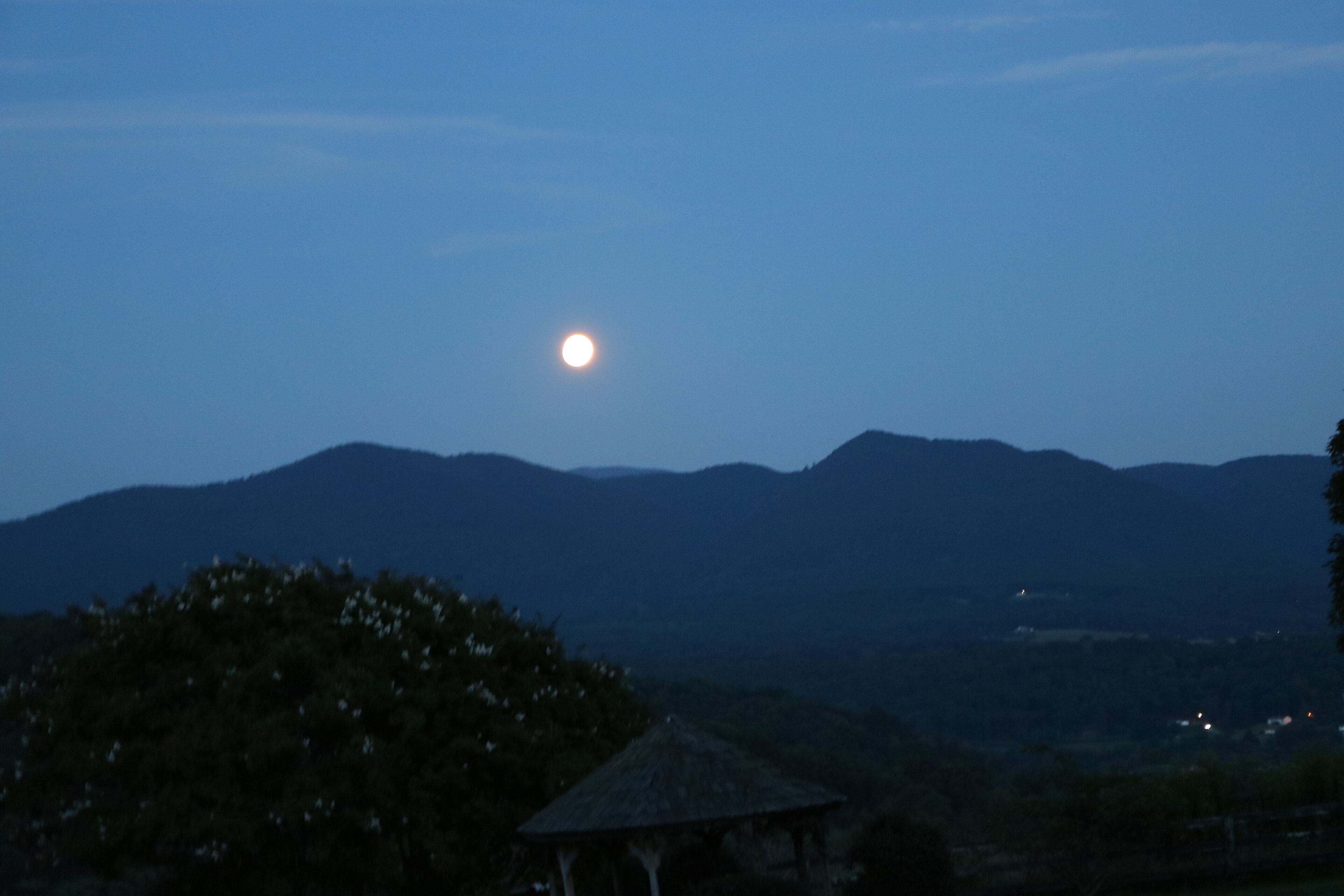 Une vue nocturne d’un paysage montagneux illuminé par la lune, avec un belvédère au premier plan.