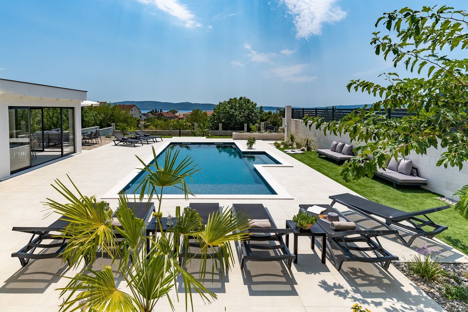 A modern outdoor pool area with a rectangular pool, lounge chairs, and a seating area with a view of the surrounding landscape.