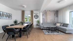 A modern living room with a grey sofa, a wooden dining table with chairs, and a large clock on the wall. - Villa Marisa with 51sqm heated, private pool, 5 bedrooms, 4 bathrooms, summer kitchen, views of the Adriatic sea and town Split (Kastel Kambelovac)