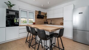 A modern kitchen with a wooden island, black bar stools, stainless steel appliances, and a large window with blinds. - Villa Marisa with 51sqm heated, private pool, 5 bedrooms, 4 bathrooms, summer kitchen, views of the Adriatic sea and town Split (Kastel Kambelovac)